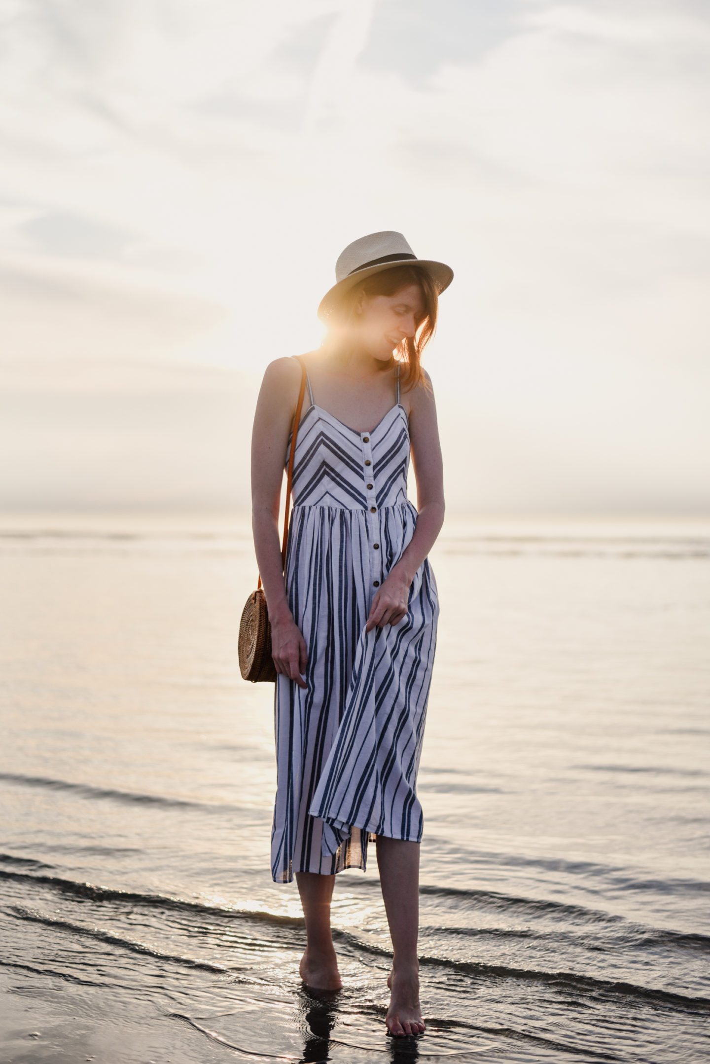 Girl in striped sundress walking in the sea during sunset