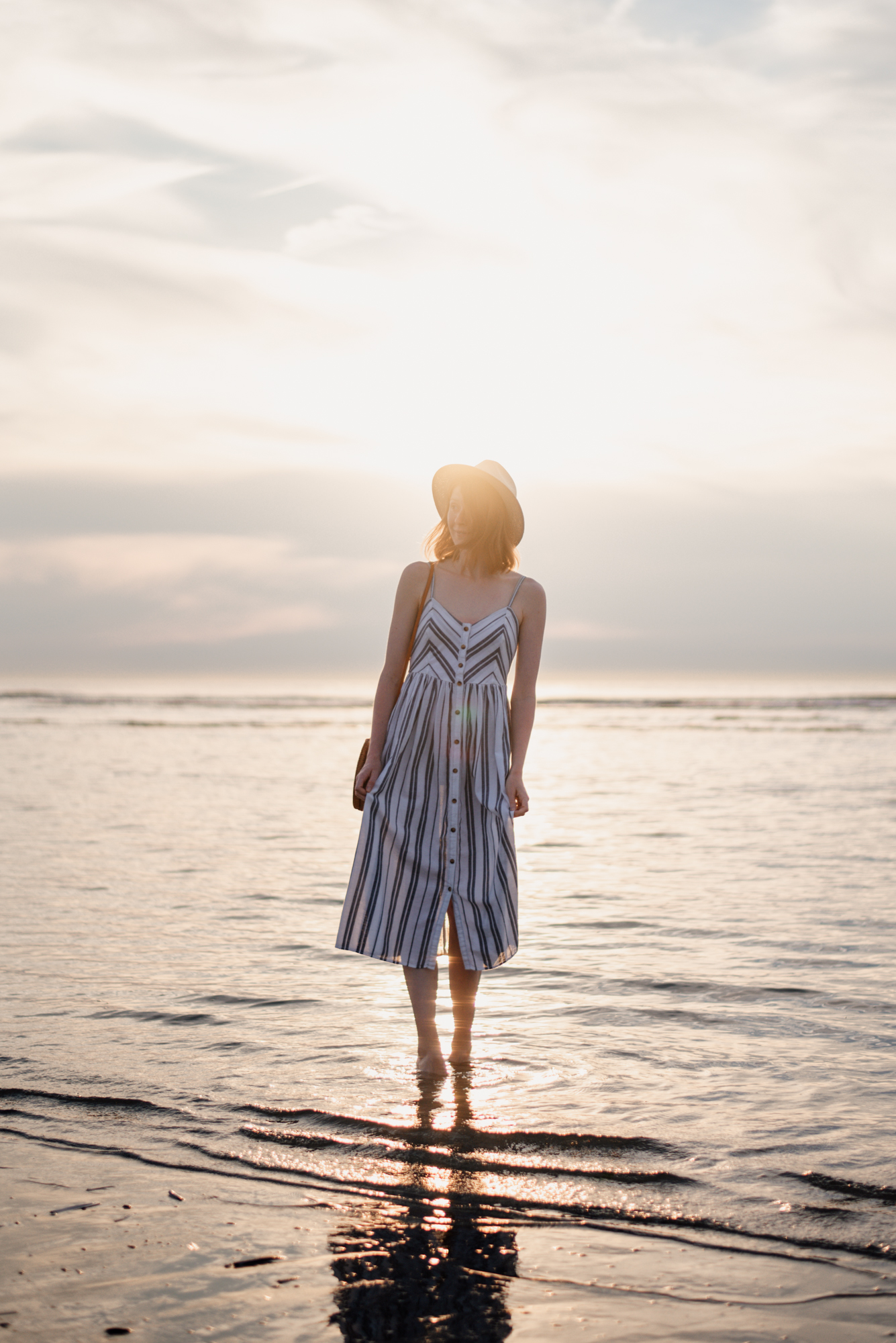 Girl in striped sundress walking in the sea during sunset