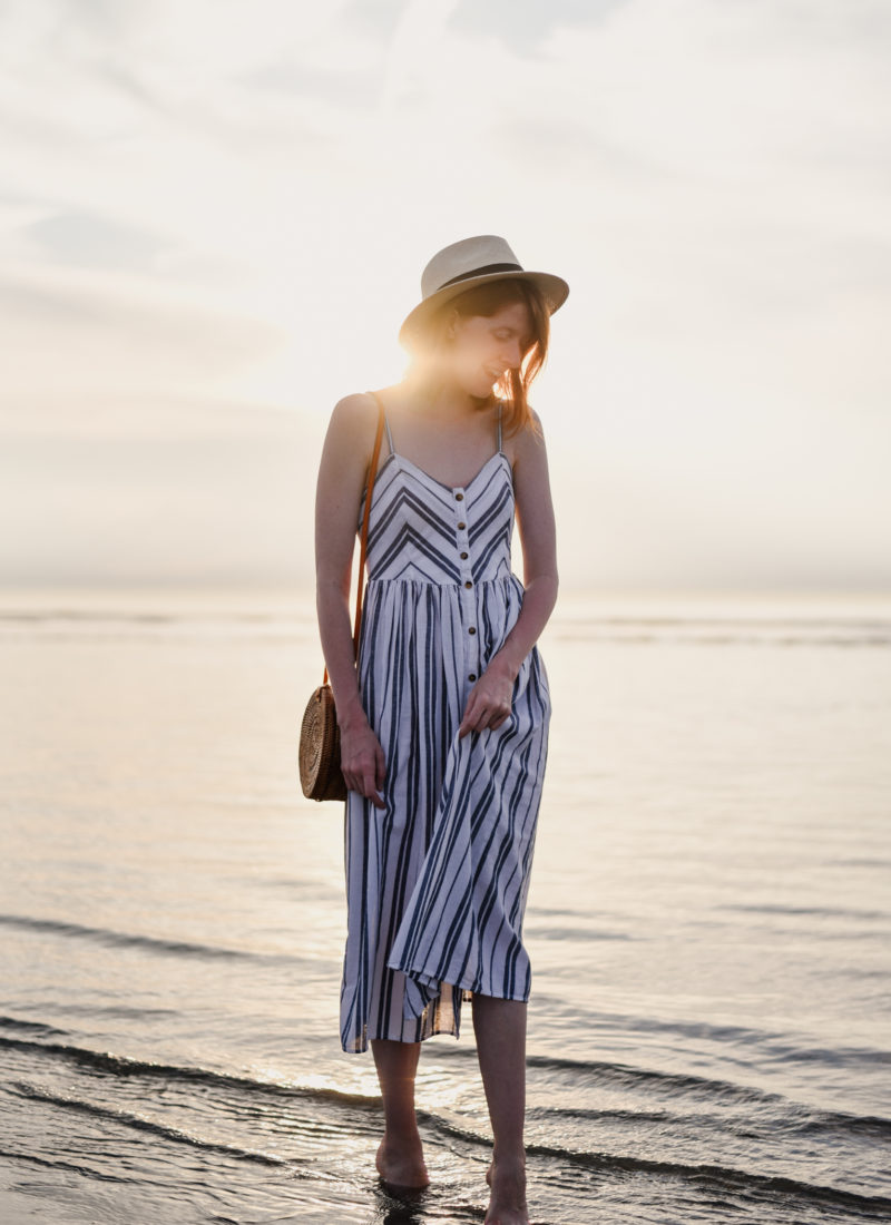 Girl in striped sundress walking in the sea during sunset