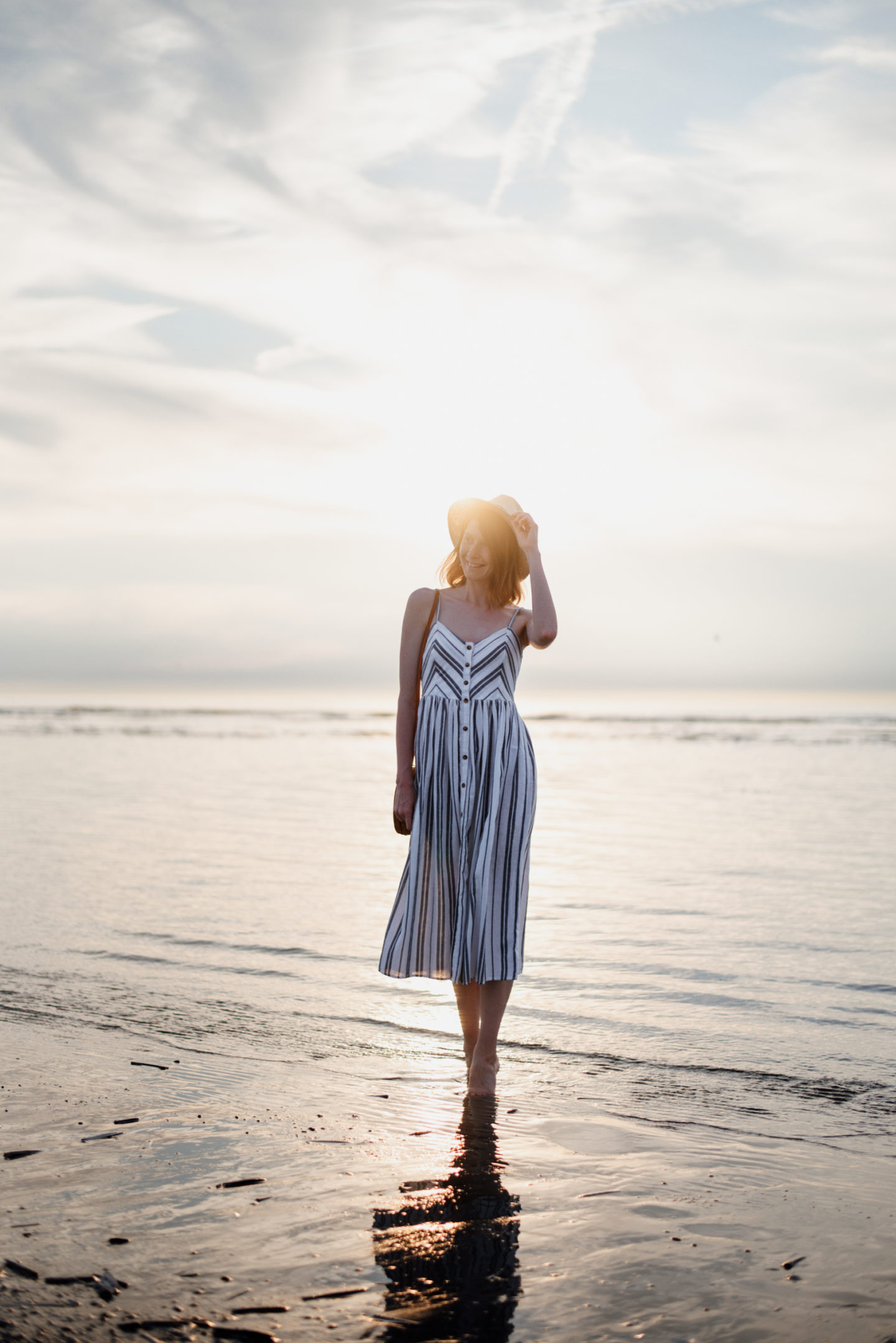 Girl in striped sundress walking in the sea during sunset