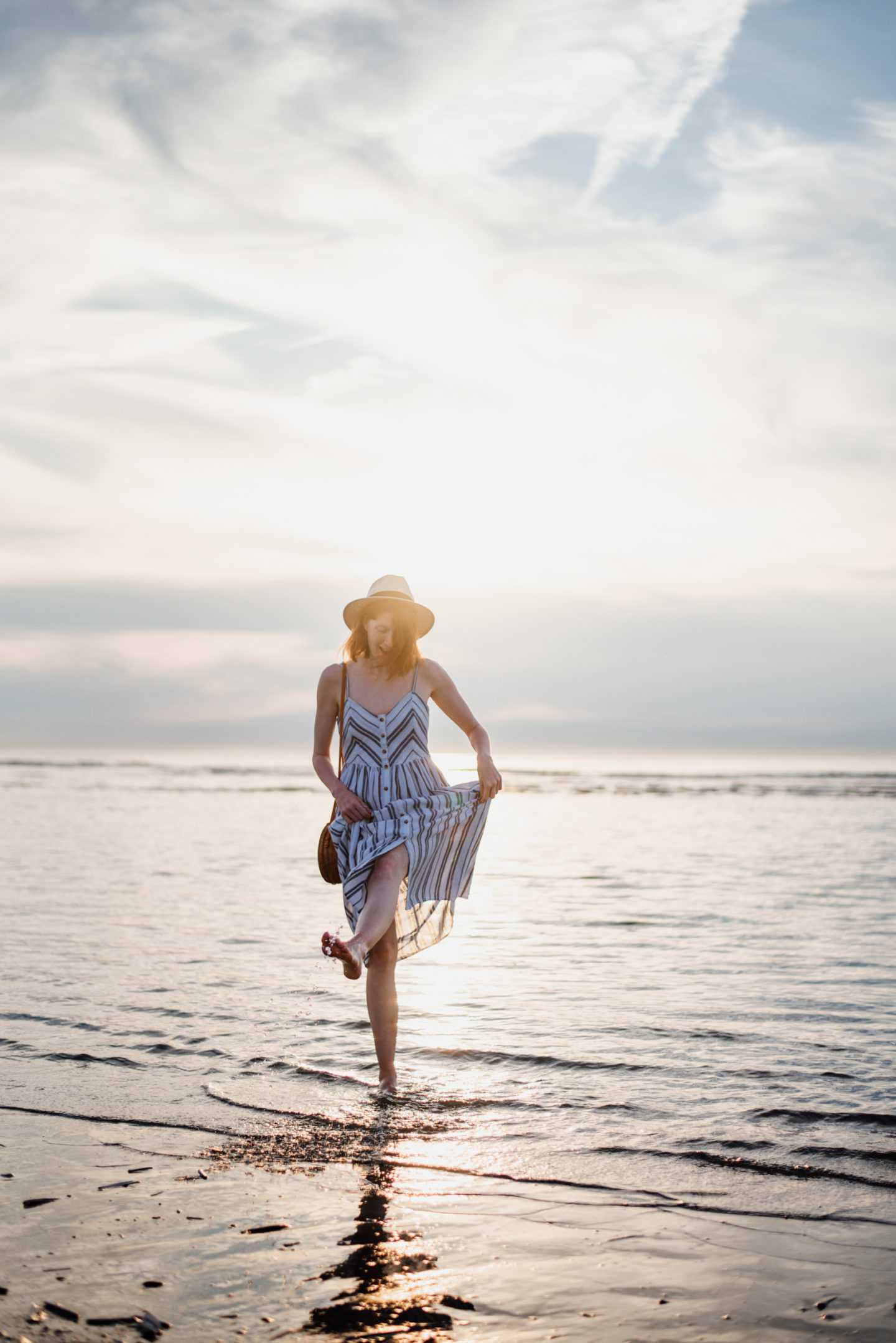 Girl in striped sundress walking in the sea during sunset