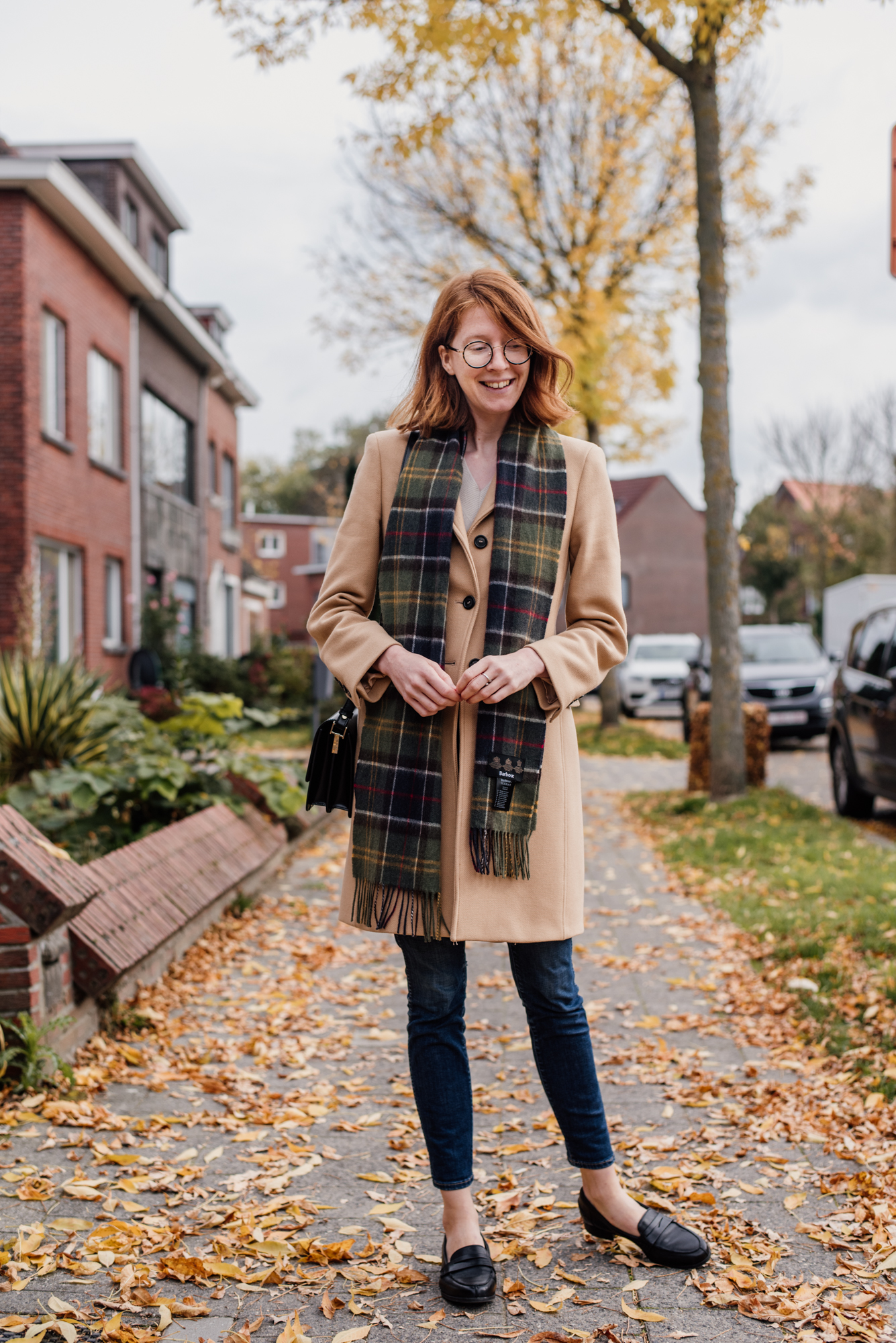 Woman wearing a camel colored coat from Zara and a plaid scarf from Barbour in an outfit for autumn