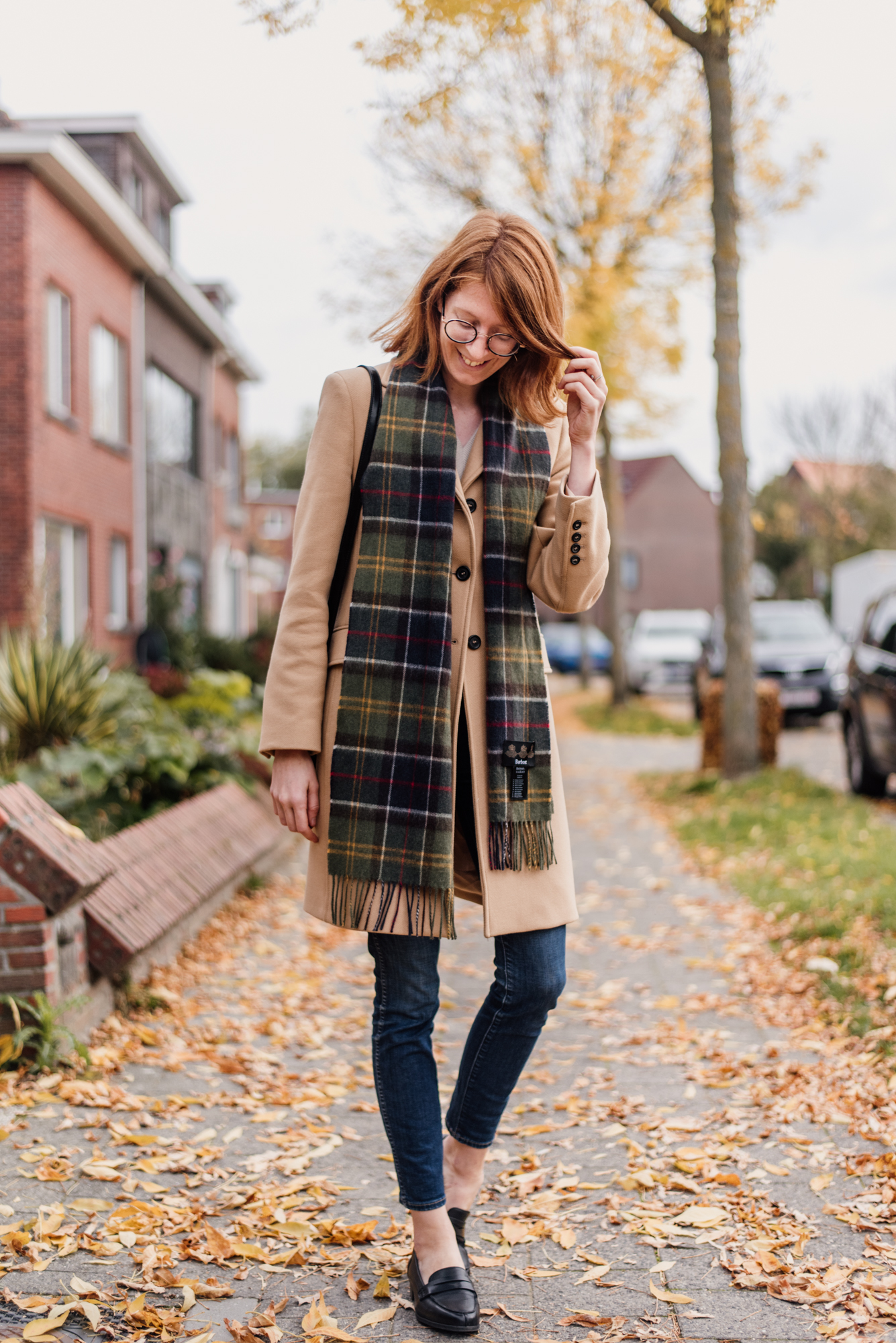 Woman wearing a camel colored coat from Zara and a plaid scarf from Barbour in an outfit for autumn