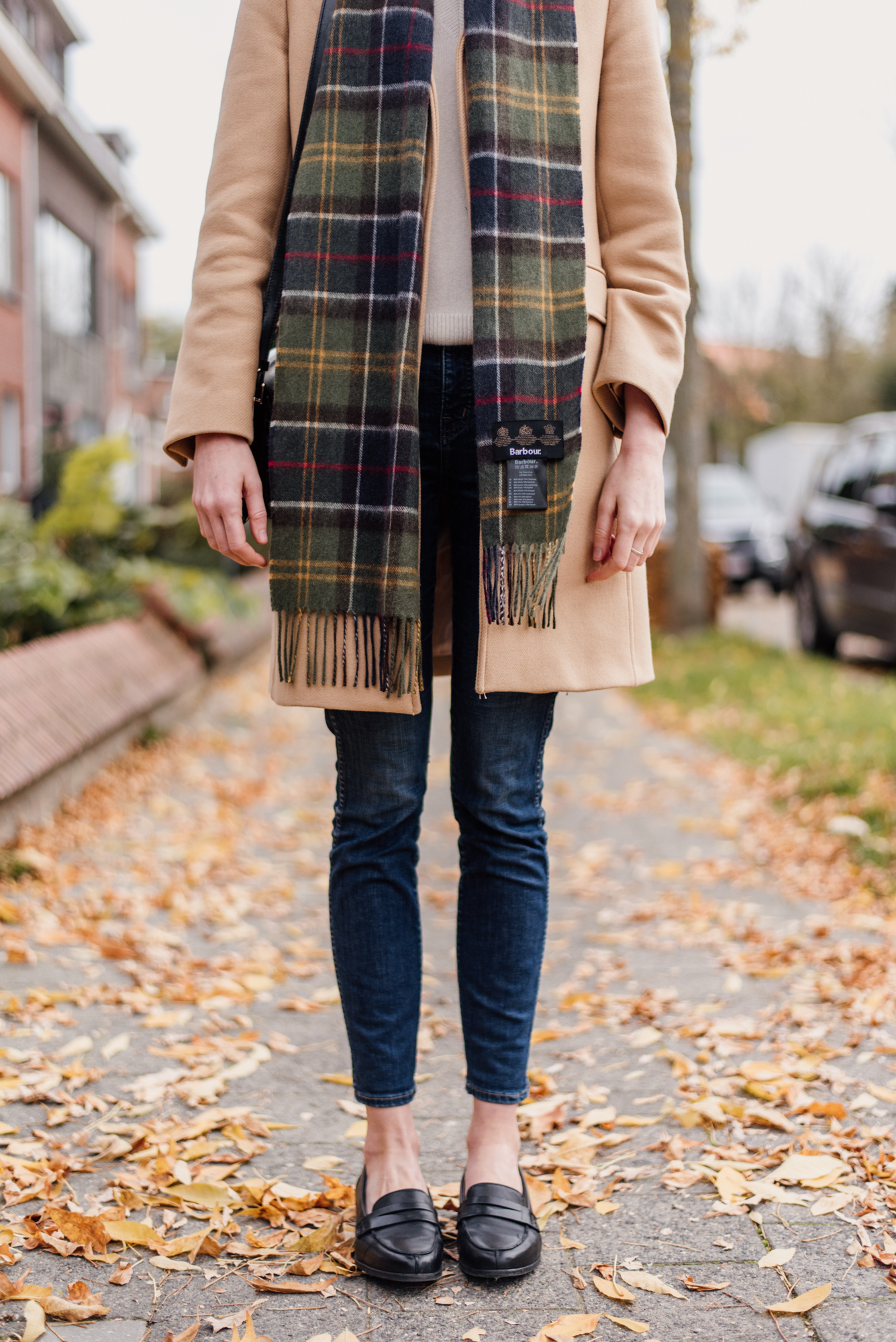 Woman wearing a camel colored coat from Zara and a plaid scarf from Barbour in an outfit for autumn